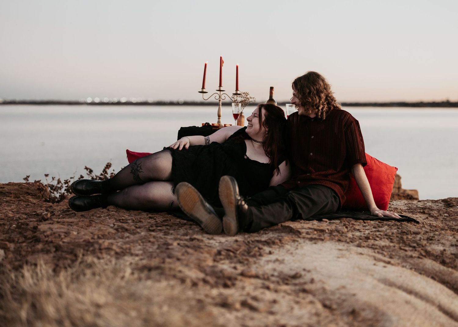 Intimate moment shared on rocky shoreline during golden hour with lake in background.