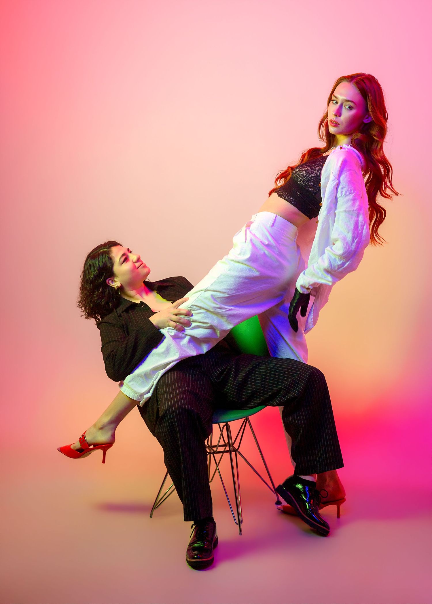 A figure in a white shirt leans back dramatically in a chair against a pink and orange gradient background.