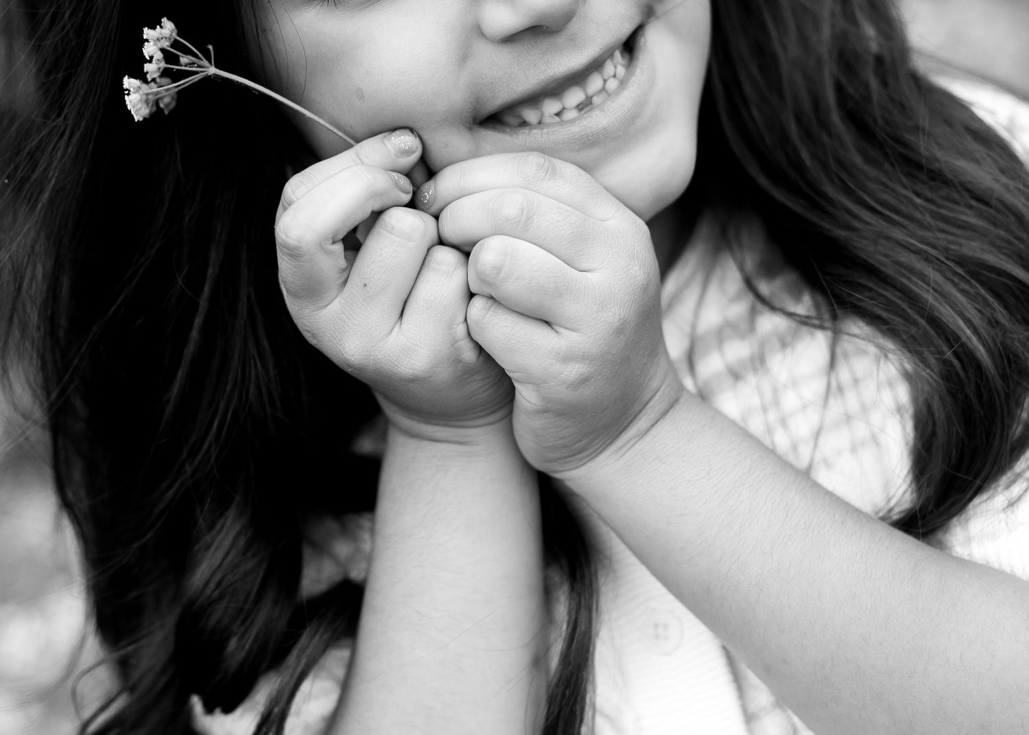Black and white photo of a smiling girl holding a small wildflower in her hands.