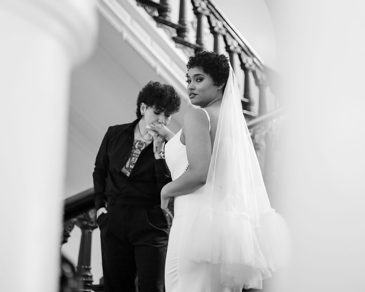Black and white photo of groom kissing brides hand on a grand staircase during wedding day.