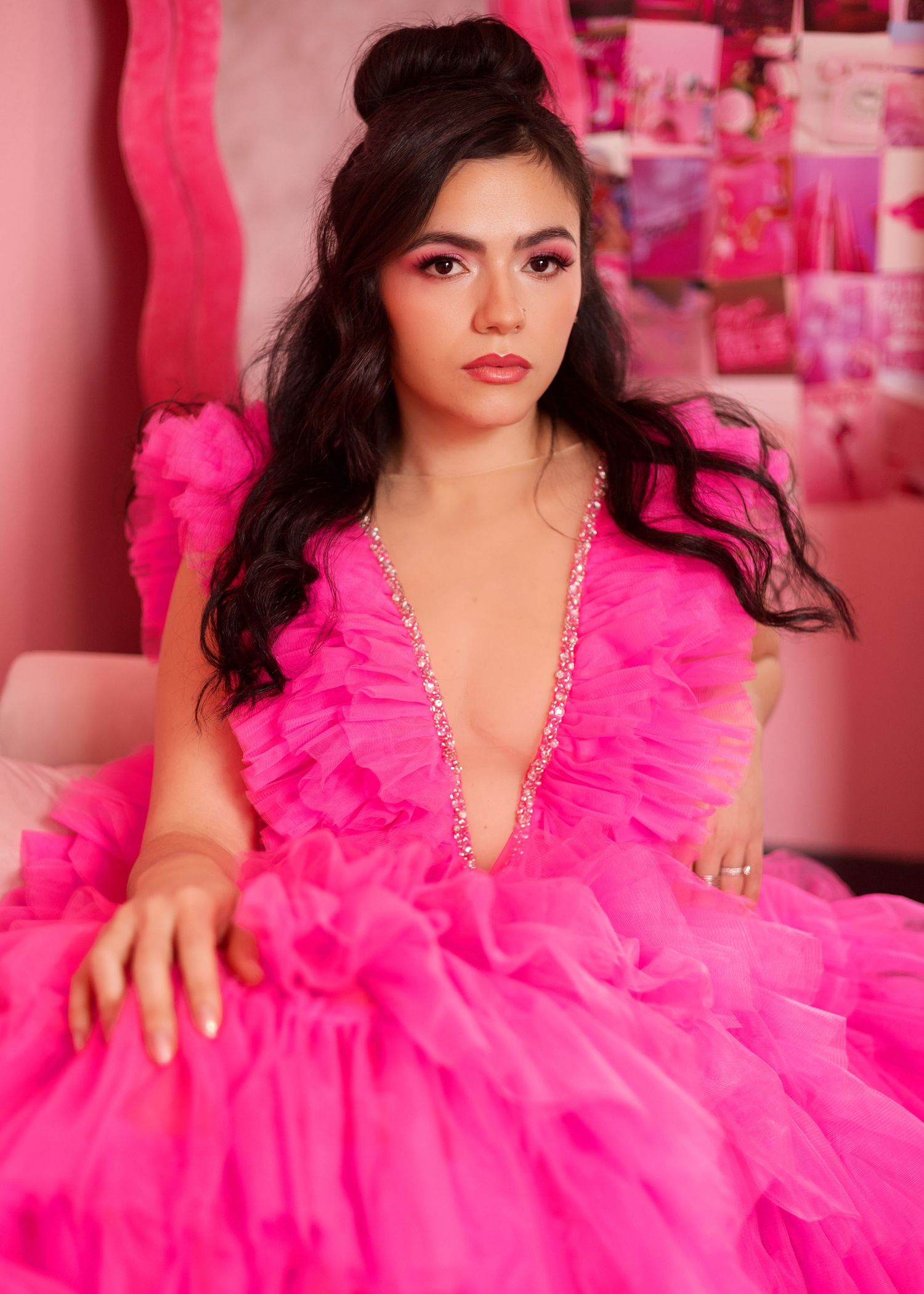 Model wearing vibrant hot pink ruffled tulle gown poses against pink studio backdrop.