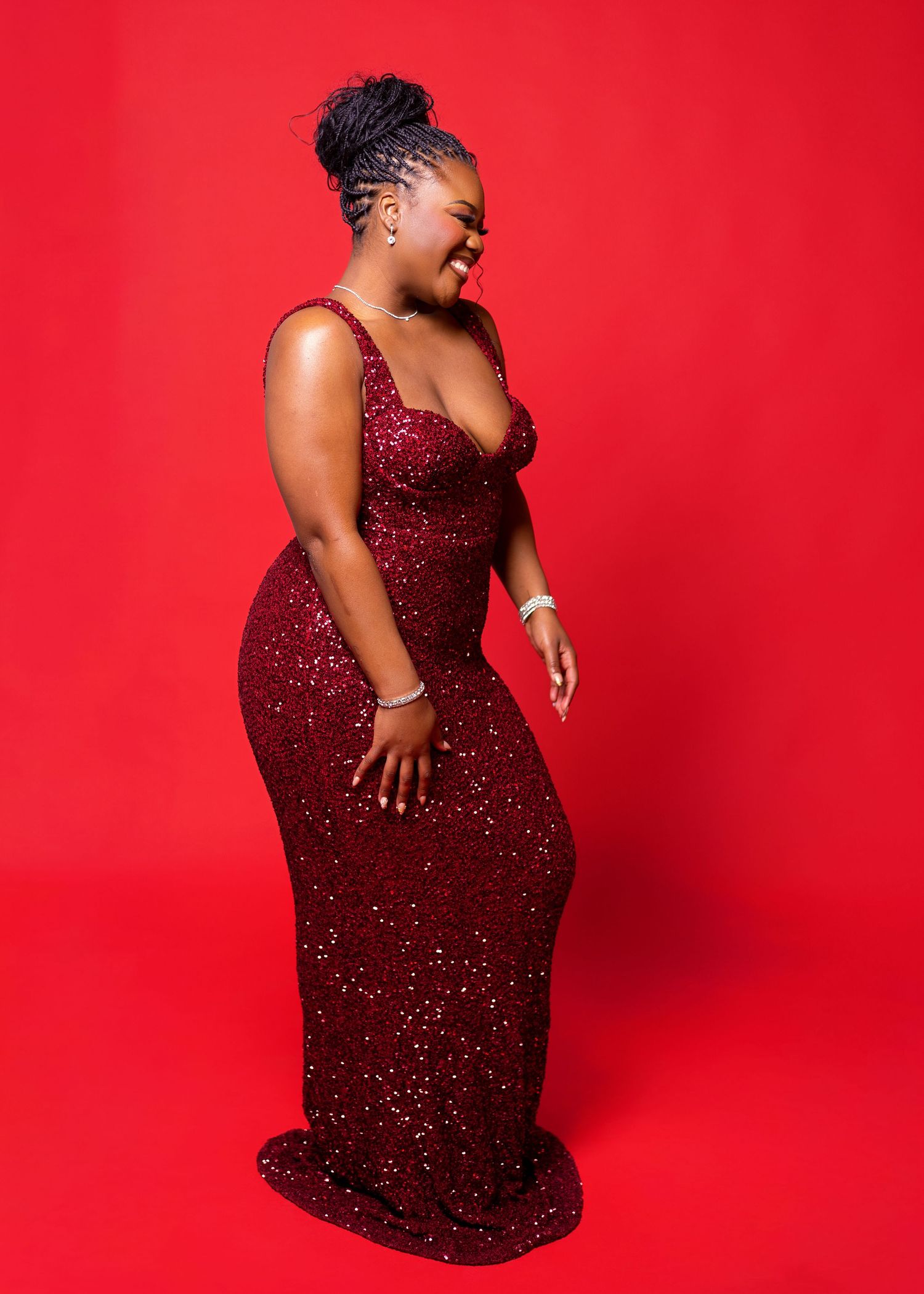 A person in a sparkly burgundy evening gown poses dynamically against a bright red backdrop.