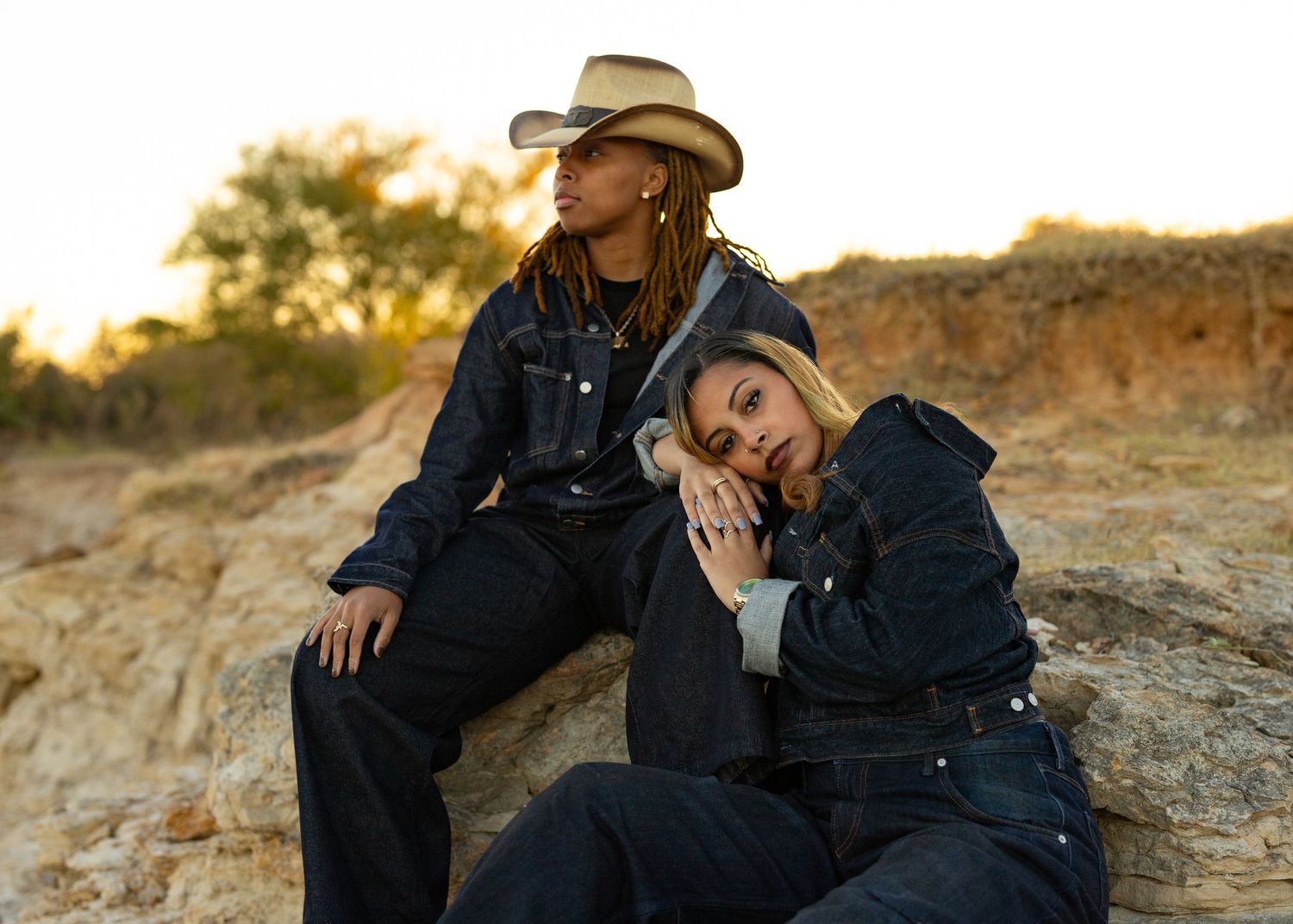 Romantic couple in dark clothing and cowboy hat sharing tender moments on rocky terrain at sunset.