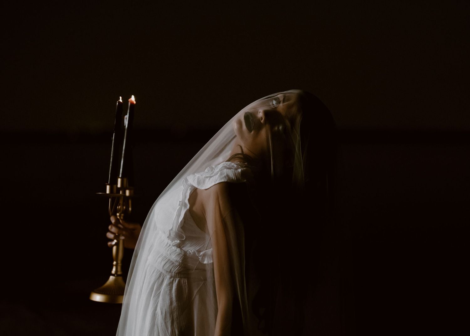 Moody silhouettes of a bride in dark lighting with candles creating atmospheric shadows.