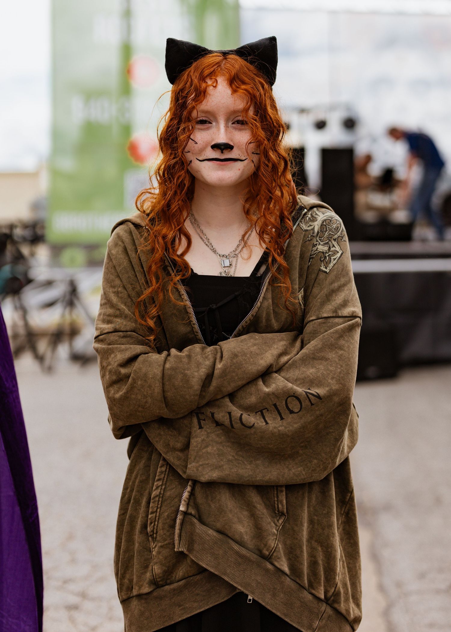 Person in brown jacket with fox-like face paint and red hair poses outdoors.