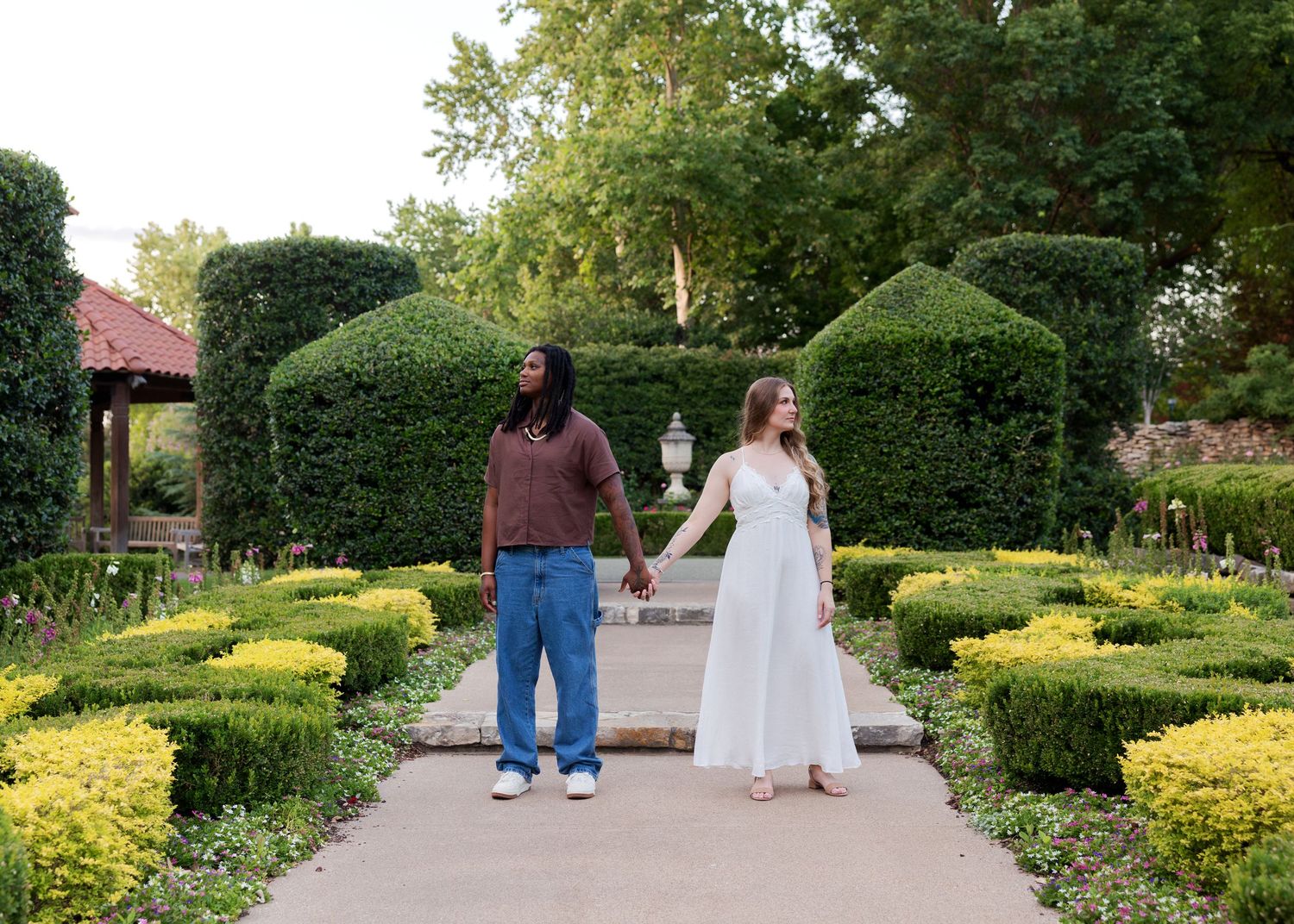 Couple holding hands in a formal garden with manicured hedges, yellow flowers, and topiary bushes.