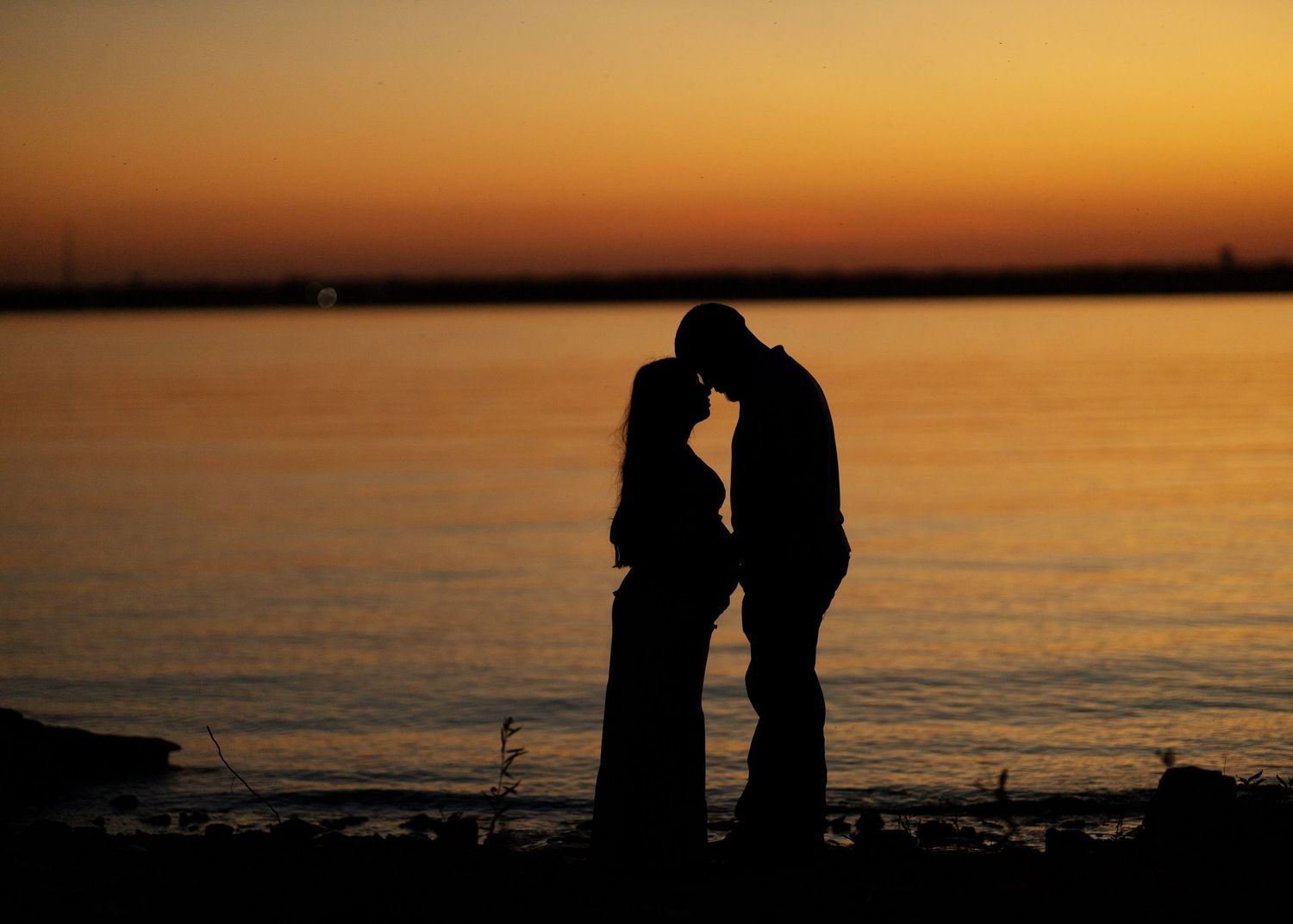 Silhouettes against vibrant orange sunset over calm water.