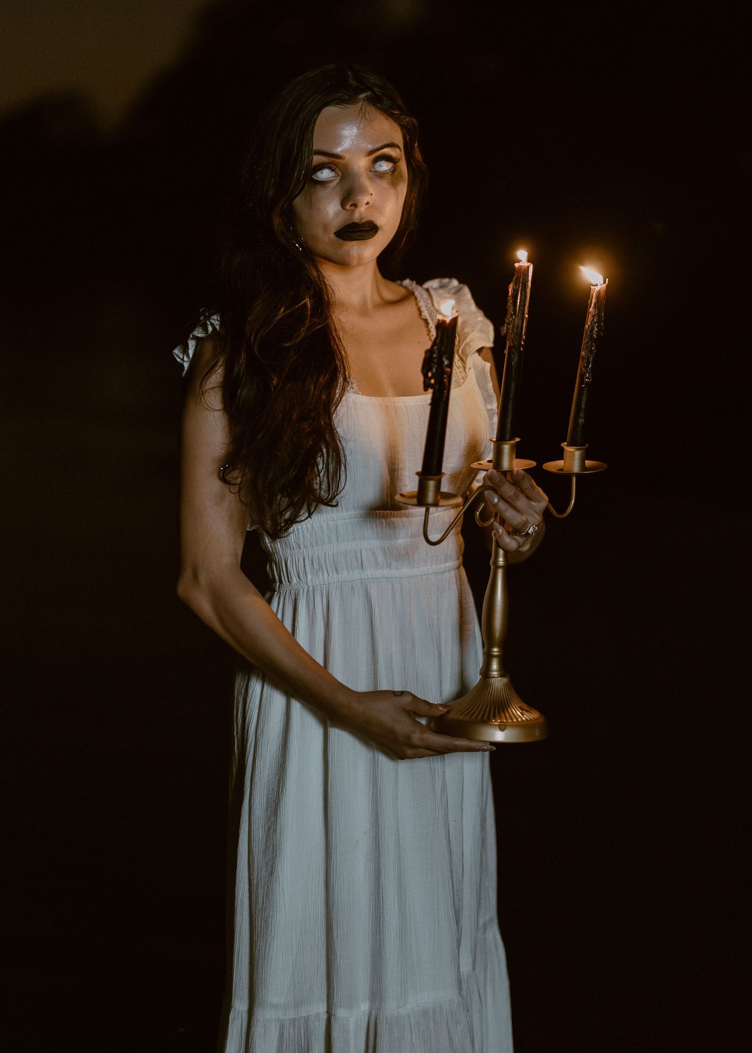 Atmospheric nighttime photography with white dress, candles and vintage-inspired styling in dark setting.