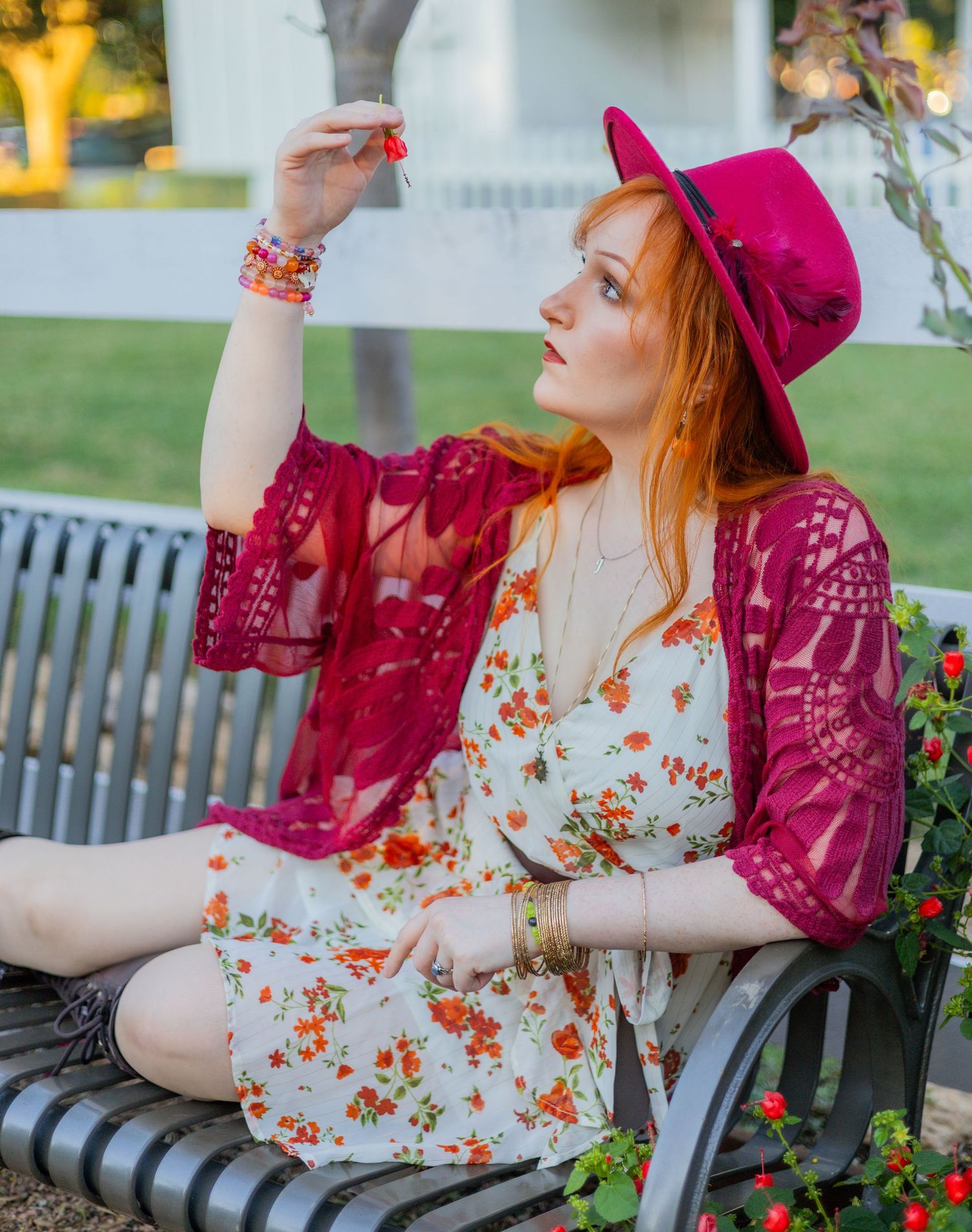 A romantic garden photoshoot showcases a floral dress and burgundy accessories on a bench.