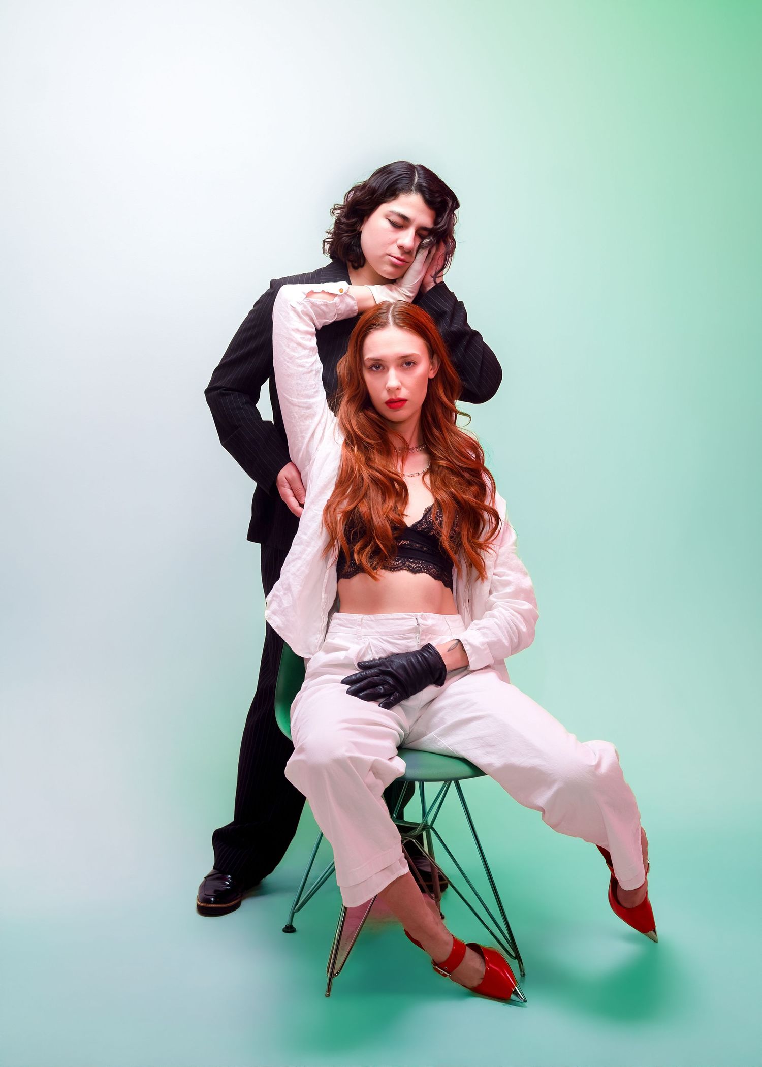 Two models pose in contrasting black and pink outfits against a mint green backdrop for a fashion photoshoot.