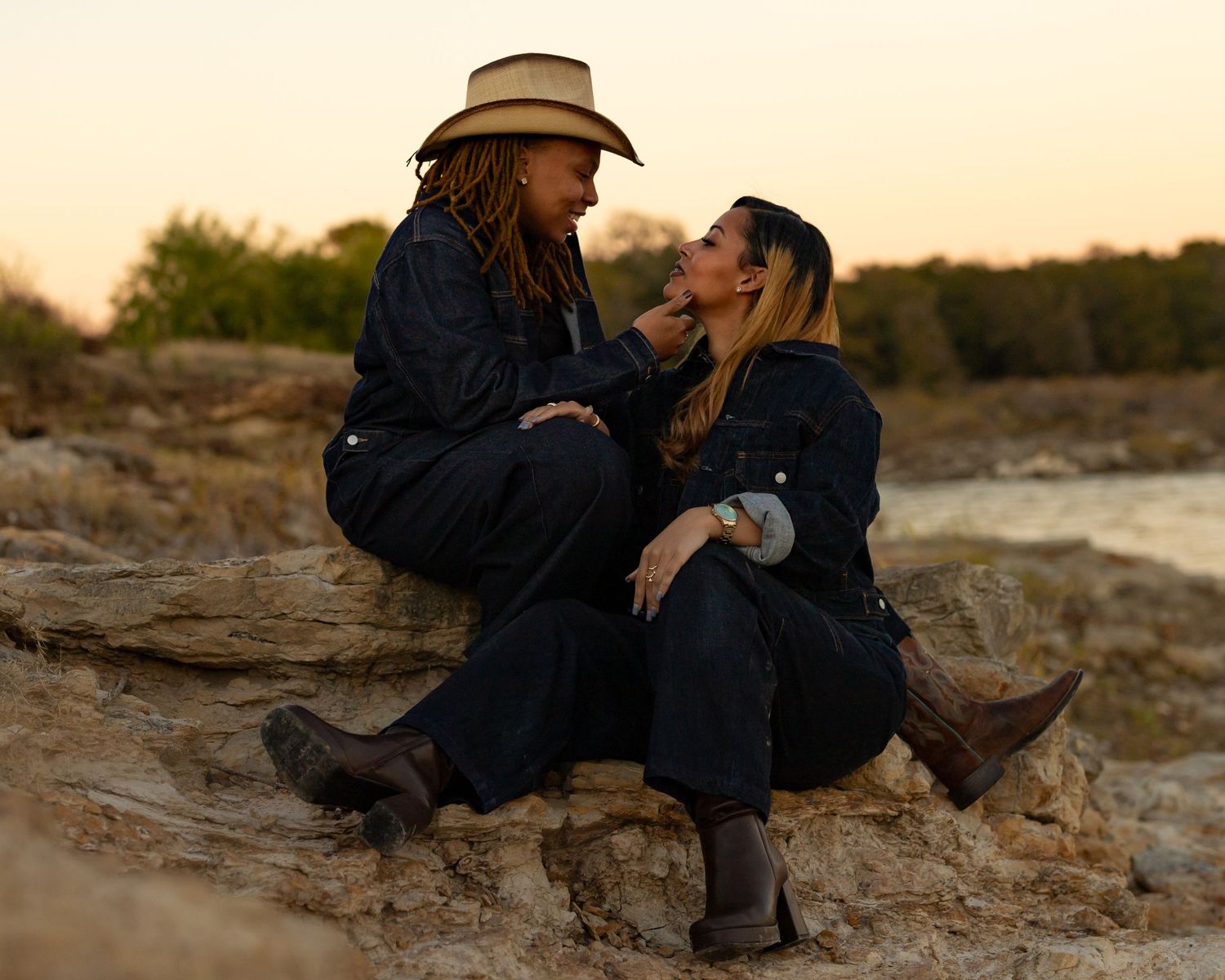 Couple in western attire sharing affectionate moments on rocky terrain during sunset.