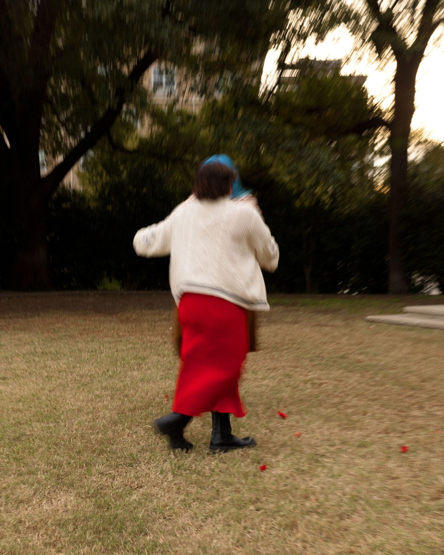 People playing with red petals scattered on grass during a sunny afternoon.
