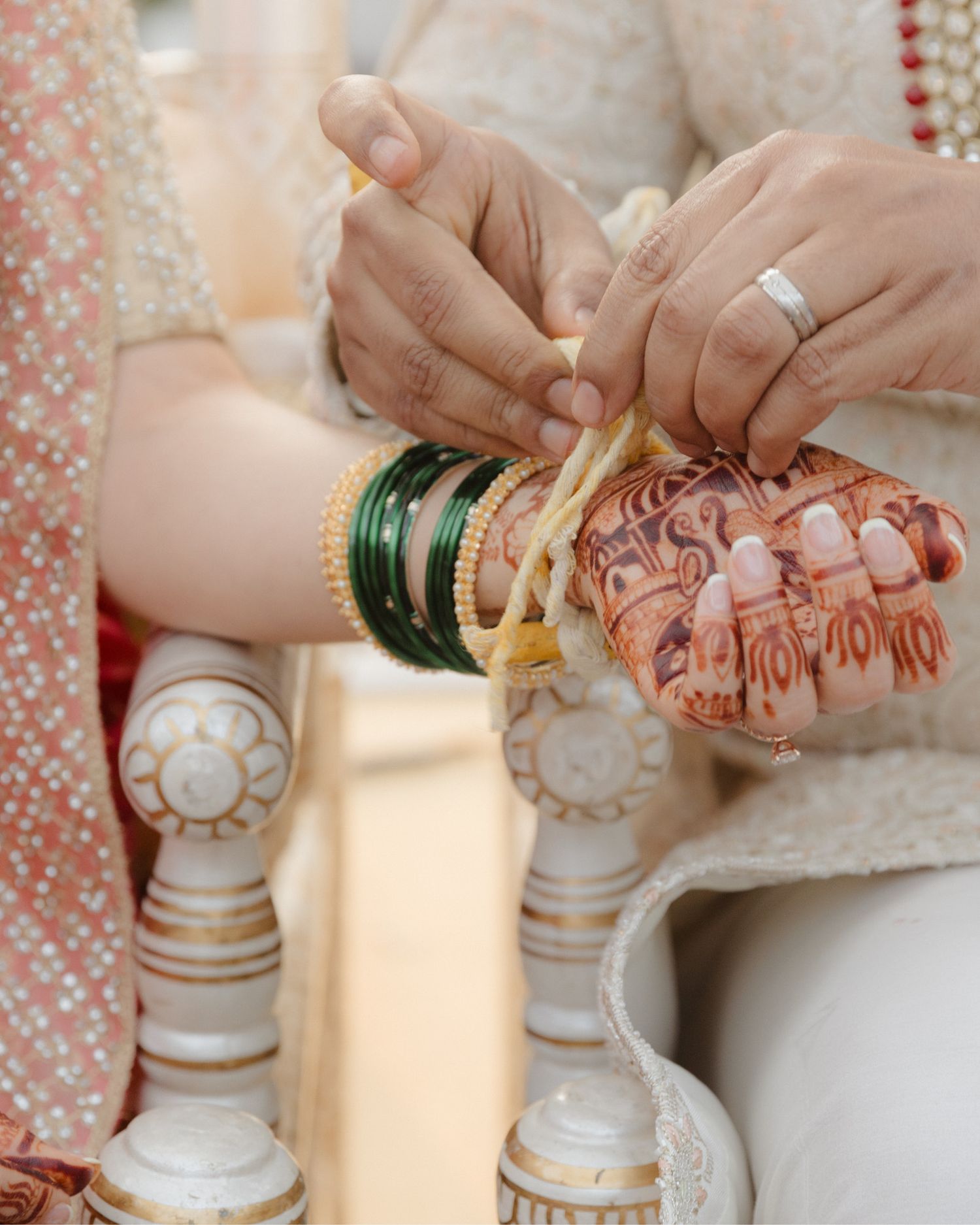 Close-up of Indian bride and grooms hands during wedding ceremony, bride wearing green bangles and mehndi.