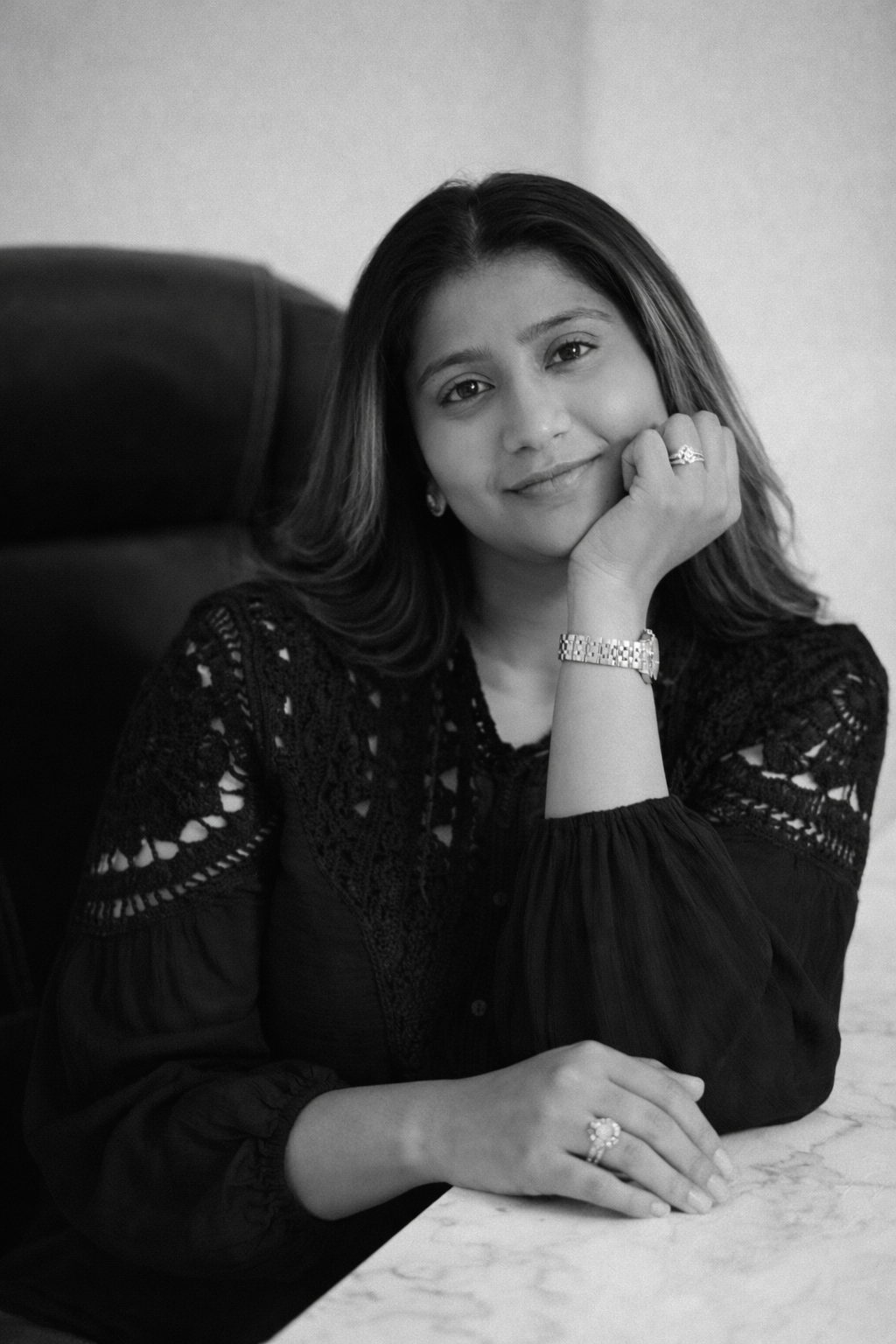 Black and white portrait of a smiling South Asian woman resting chin on hand.
