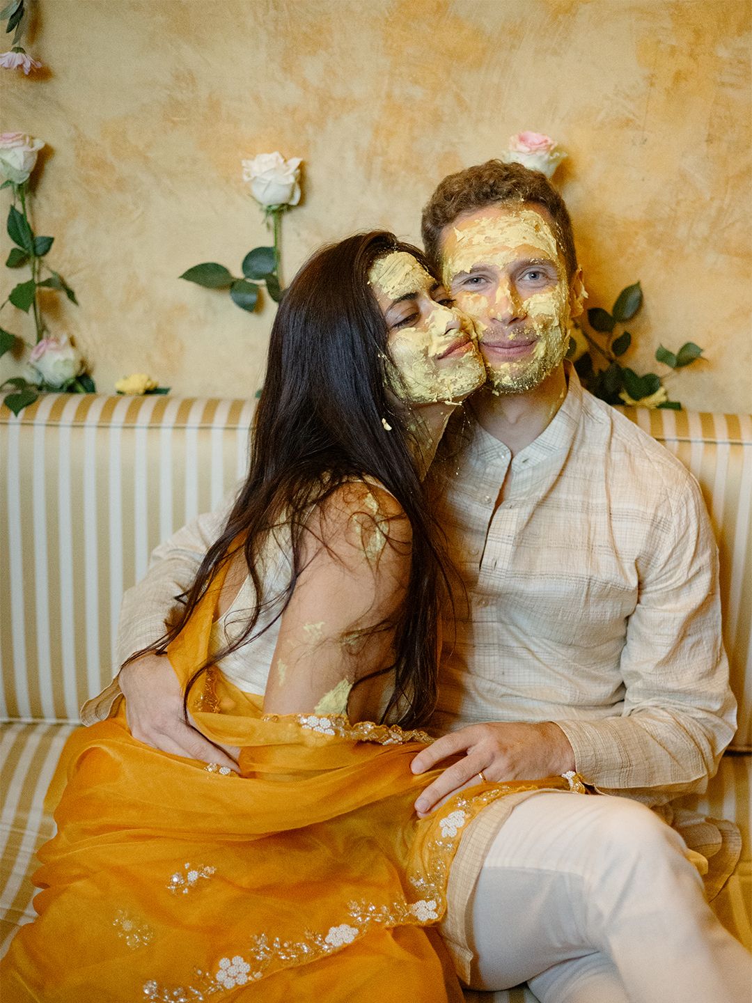 Couple with turmeric haldi paste on faces during Indian wedding pre-ceremony celebration, bride in orange lehenga.