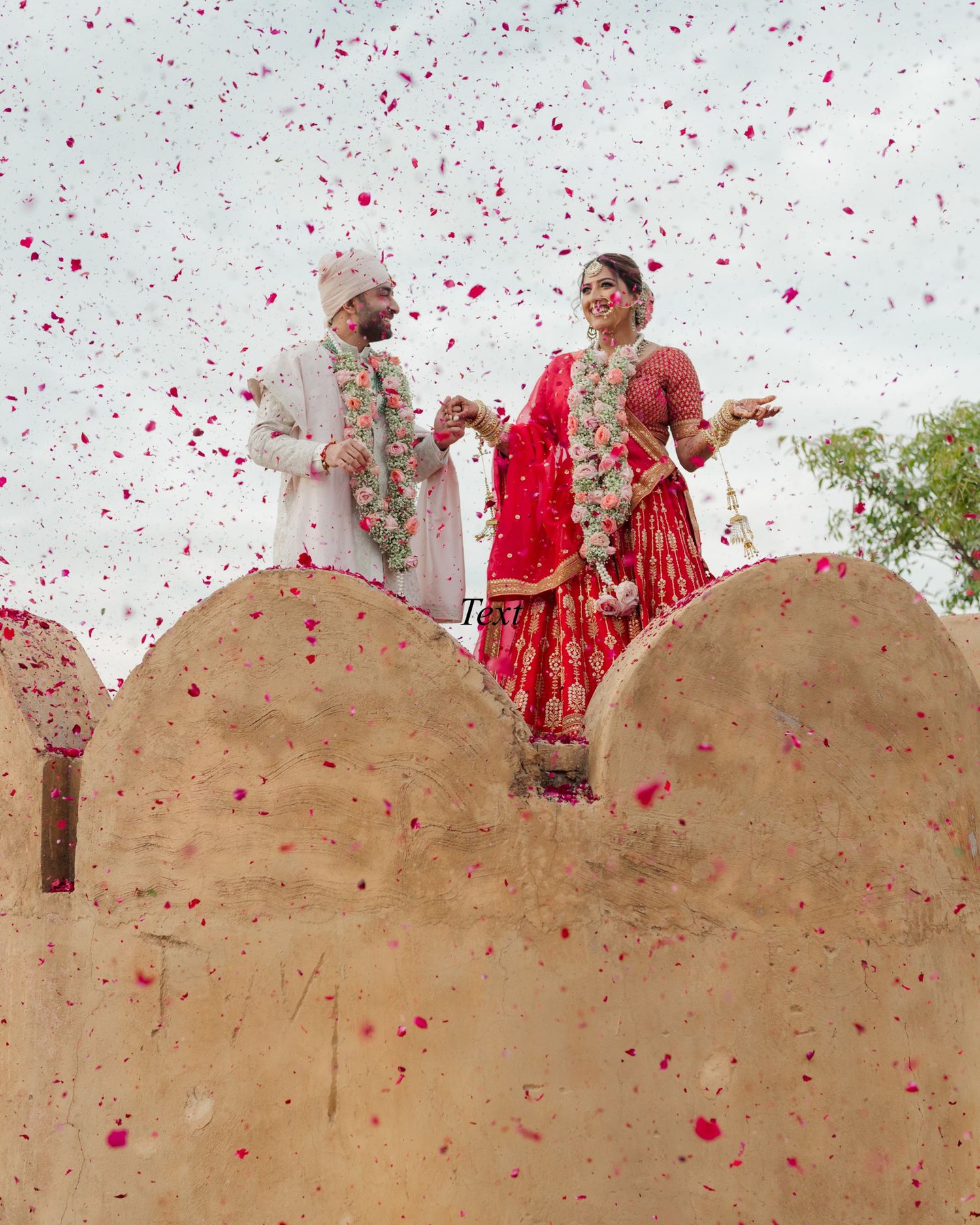 Indian bride and groom celebrating with red flower petals confetti on a rooftop at their wedding.