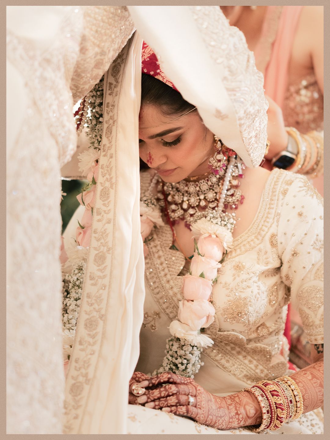Indian bride in ivory lehenga with polki necklace holding floral garland during wedding ritual.