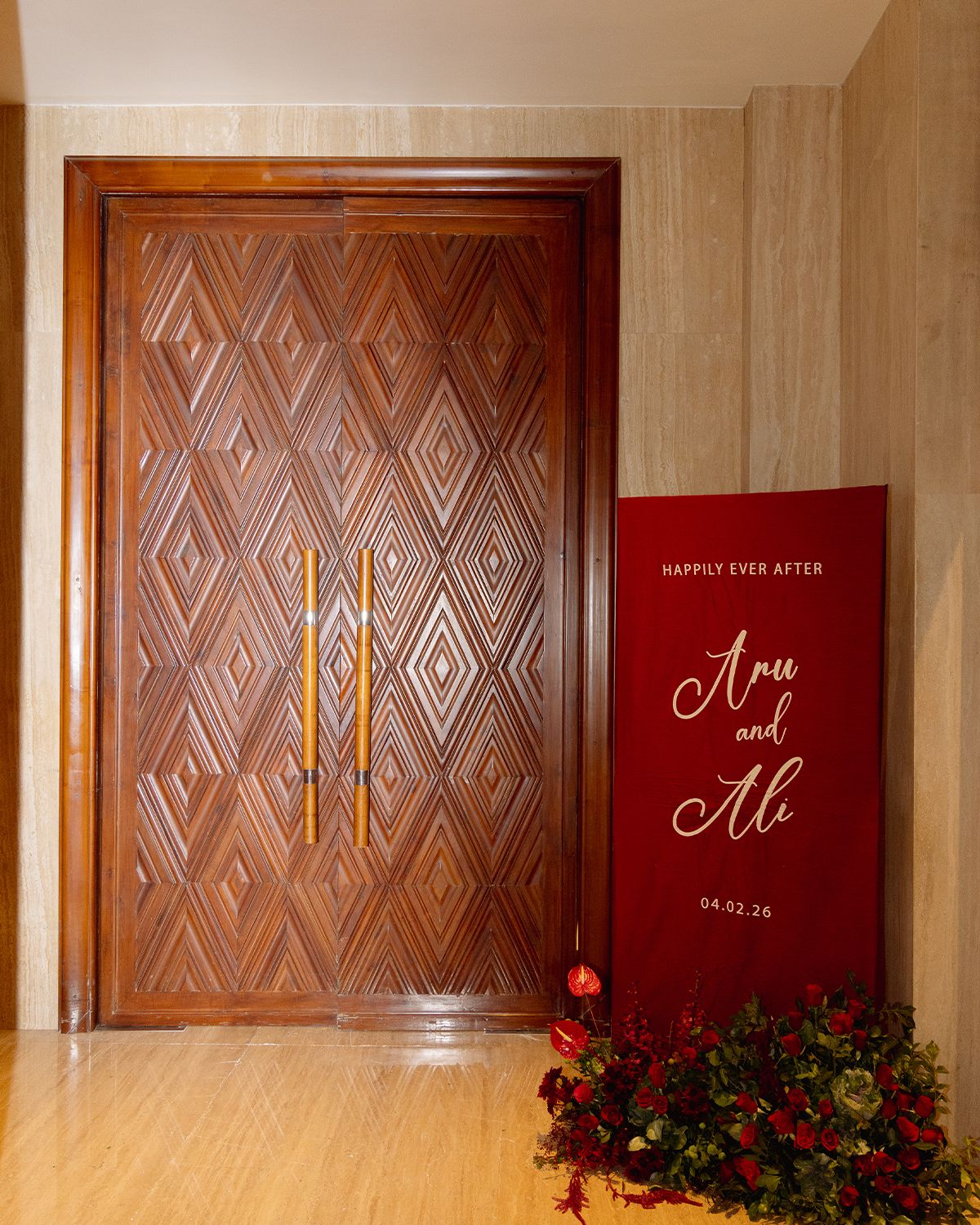 Elegant wooden door with diamond pattern beside a red wedding sign reading Happily Ever After Aru and Ali 04.02.26.