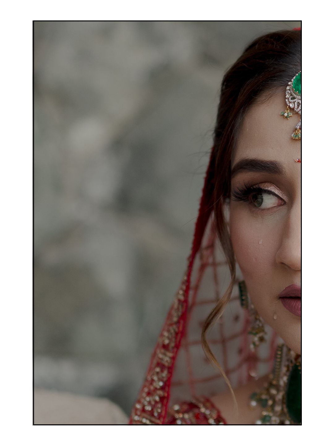 Close-up portrait of Indian bride wearing red dupatta and emerald green maang tikka with traditional jewelry.