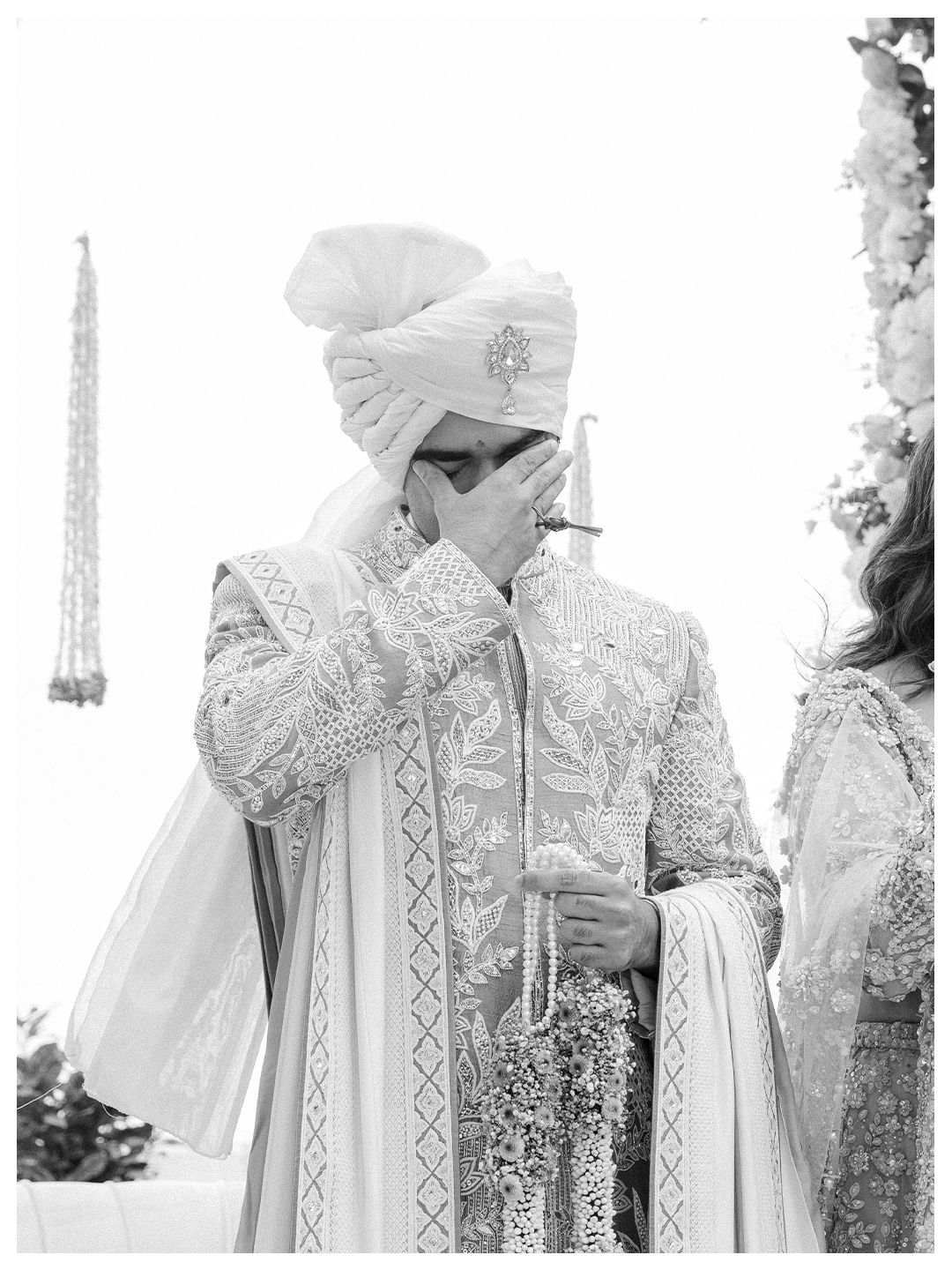 Emotional Indian groom in white sherwani wiping tears during his wedding ceremony in black and white.