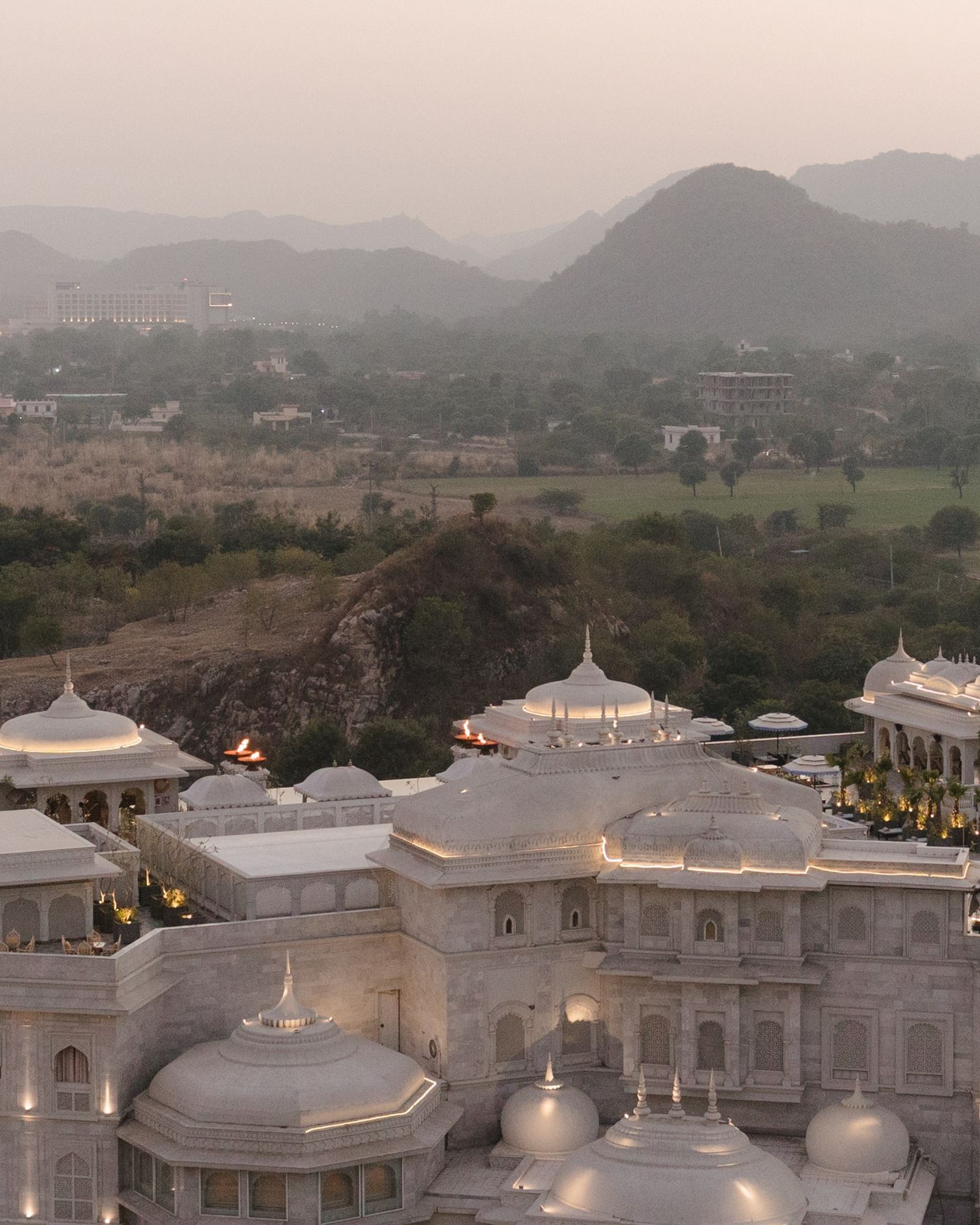 Aerial view of a grand white marble palace venue at dusk with misty mountains in the background.