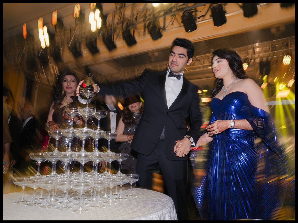 Newlyweds pour champagne tower at elegant wedding reception celebration with guests.