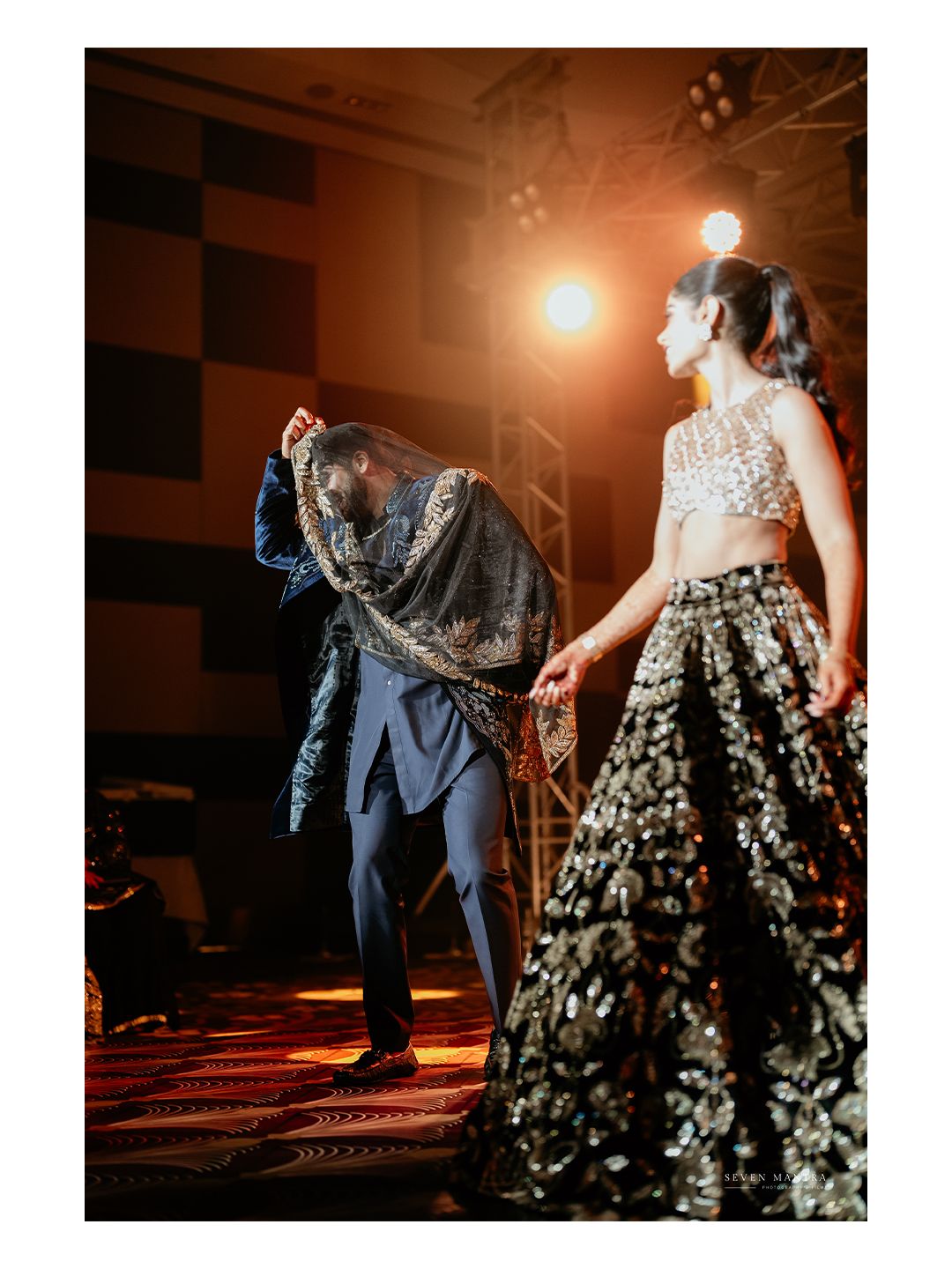 Groom in navy blue sherwani presenting dupatta to bride in embroidered lehenga on wedding stage.