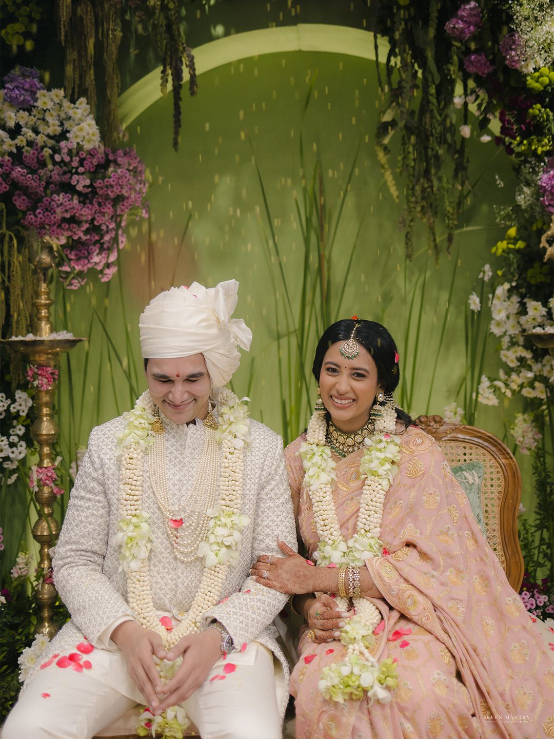 Indian bride and groom in traditional wedding attire with floral garlands at a beautifully decorated Hindu ceremony.