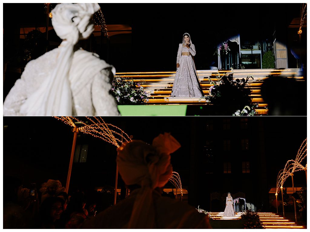 Bride makes dramatic nighttime entrance on lit staircase surrounded by sparkling wedding decor and guests.