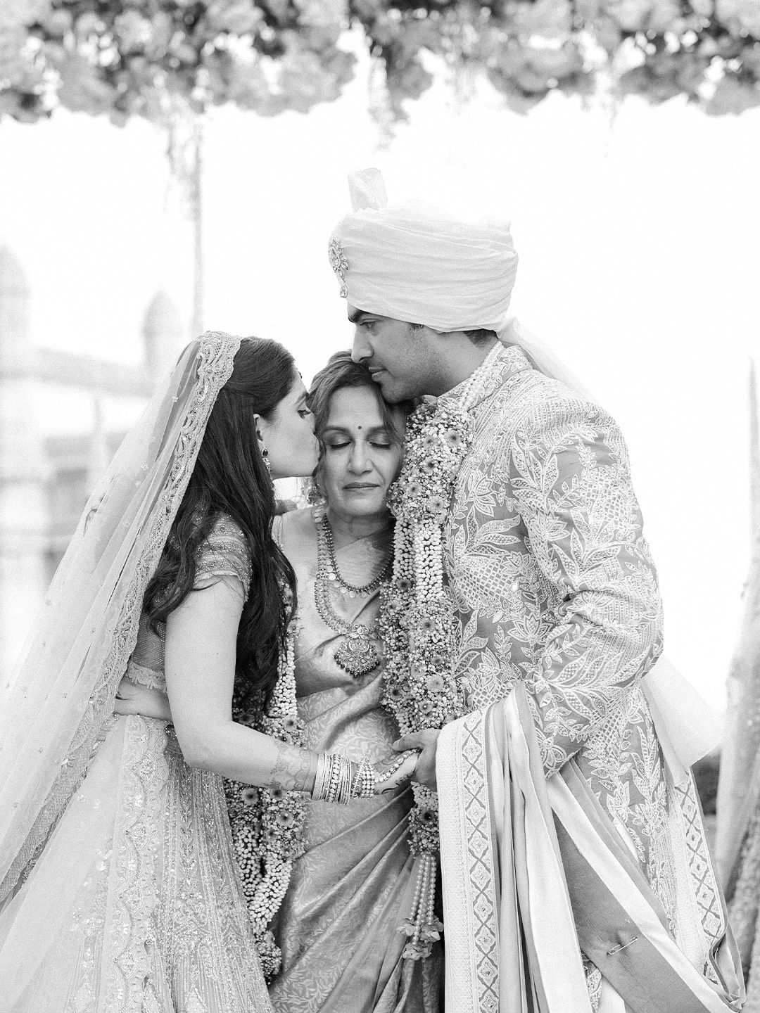 Black and white photo of Indian bride, groom, and mother sharing a tender emotional wedding moment.