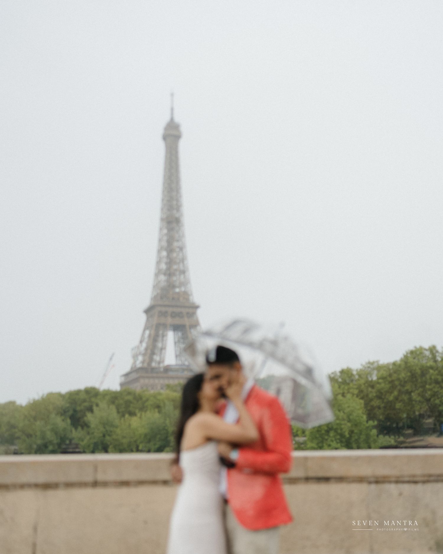 Couple sharing a romantic moment under umbrella in front of the Eiffel Tower on a rainy day in Paris.