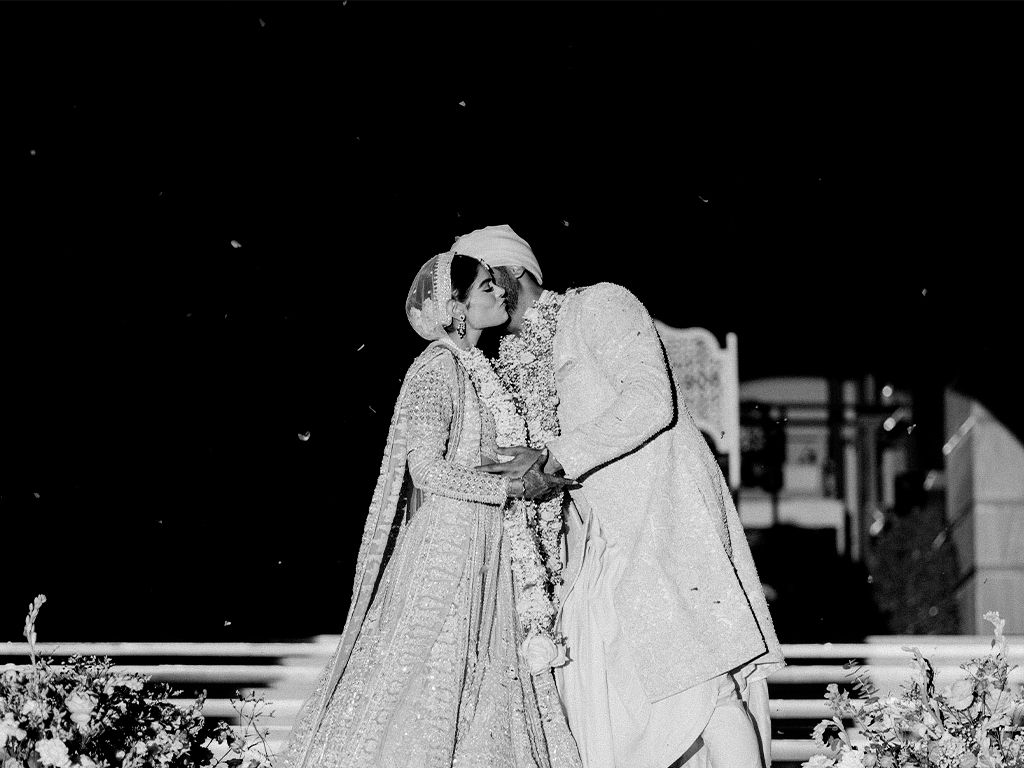 Black and white photo of Indian bride and groom sharing a kiss during outdoor wedding ceremony.