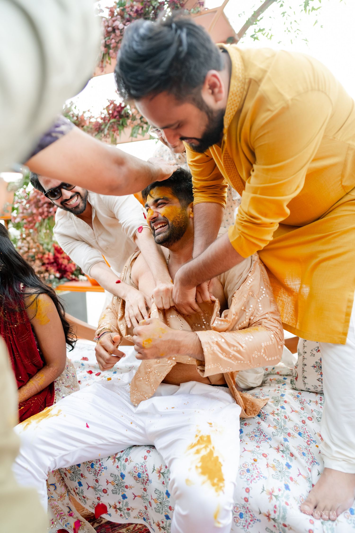 Groom laughing as friends apply haldi turmeric paste during vibrant Indian wedding ceremony celebration.