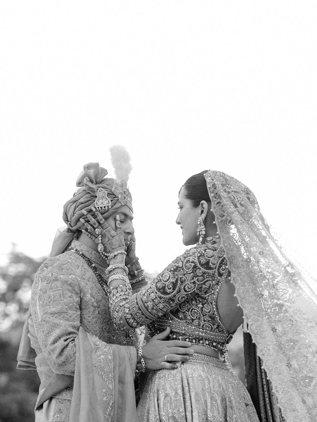 Black and white portrait of Indian bride and groom in traditional wedding attire sharing an intimate moment.