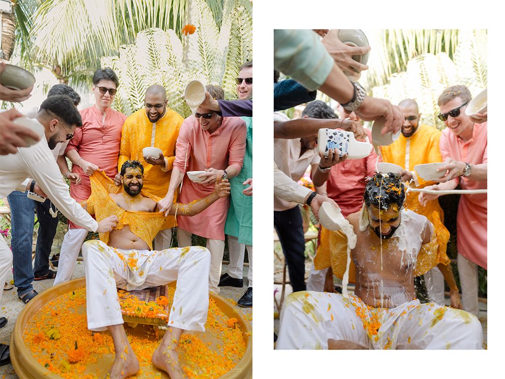 Groom sits in turmeric haldi ceremony bowl surrounded by friends pouring yellow paste during Indian wedding celebration.