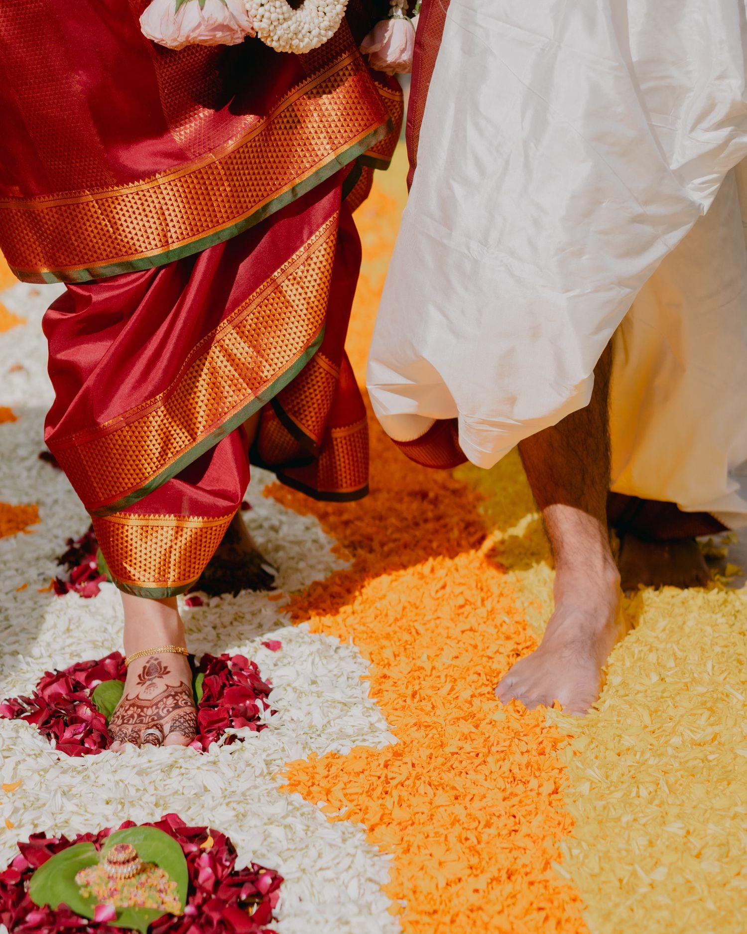Bare feet of Indian wedding couple standing on colorful flower petal rangoli during traditional Hindu ceremony.