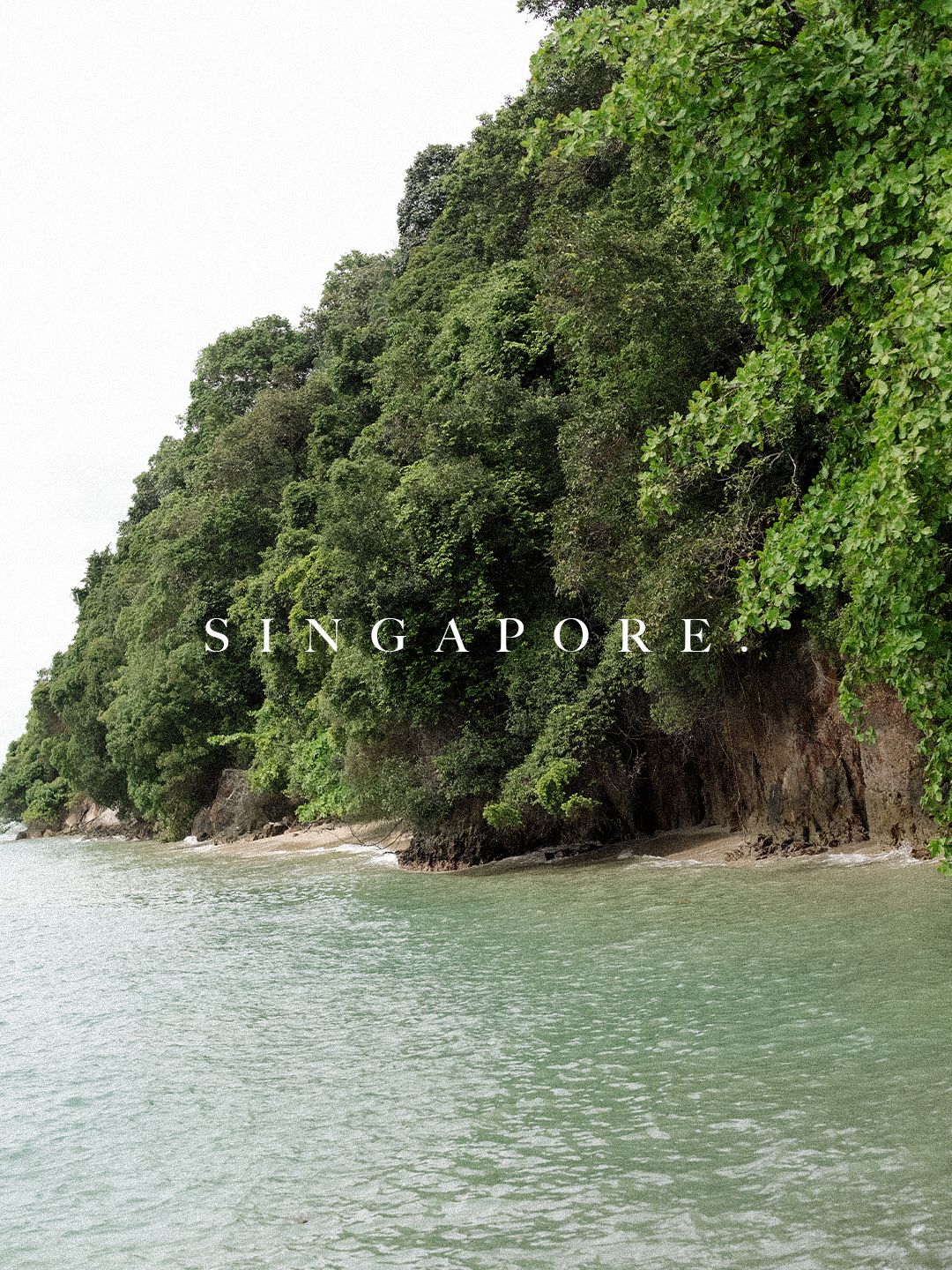 Lush green cliffside meets turquoise waters at Singapore's scenic coastal landscape.