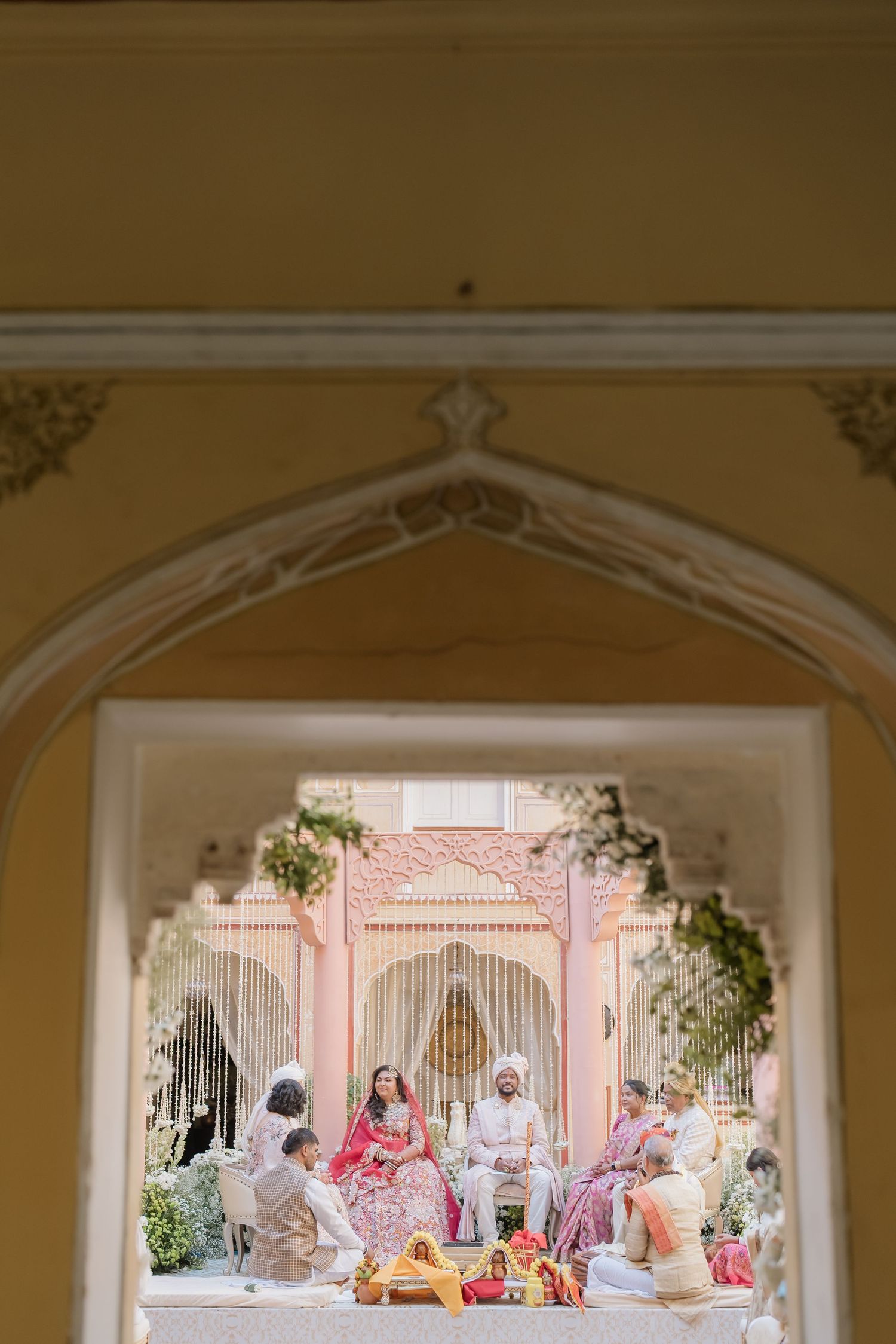 Framed view through an ornate arch of an Indian wedding ceremony taking place in a palace courtyard.