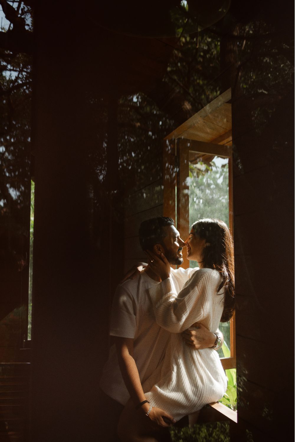 Romantic couple in white outfits share a kiss framed by a sunlit wooden cabin doorway.