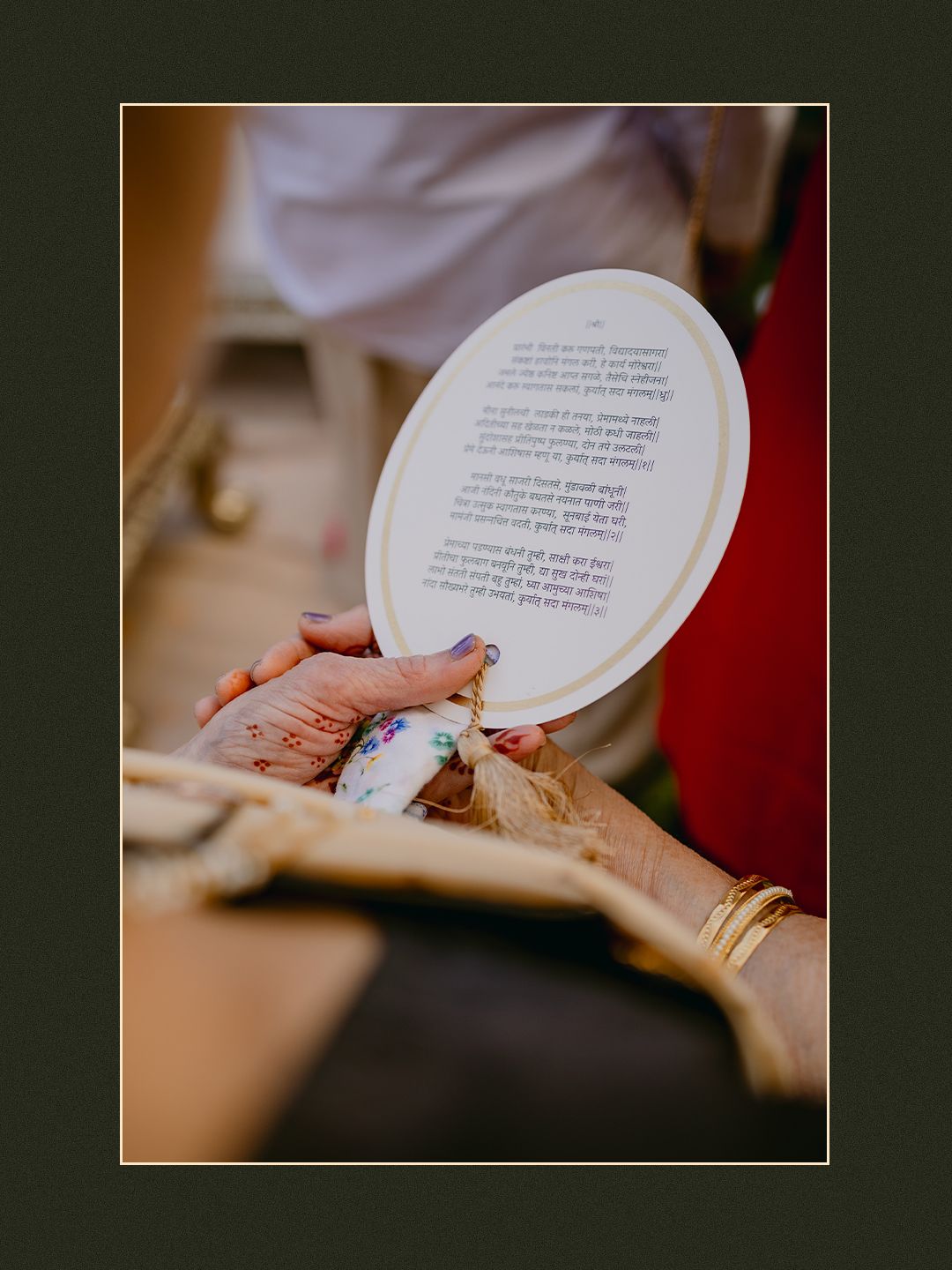 Close-up of hands holding a circular card with Sanskrit text during a traditional Indian wedding ceremony.