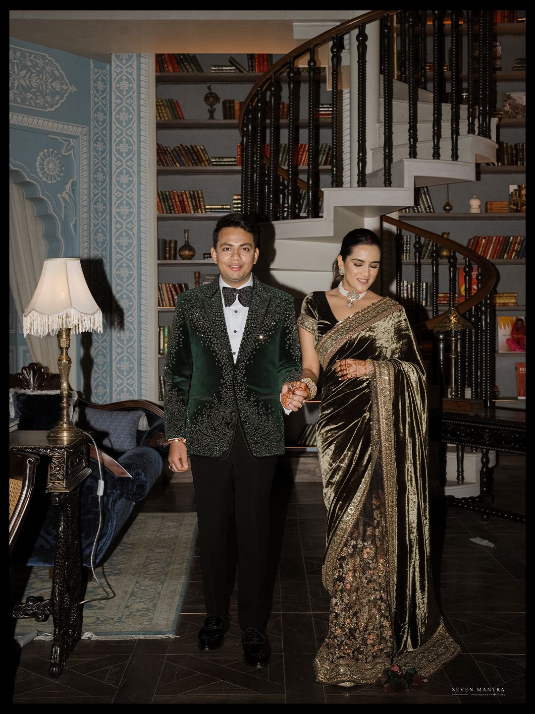 Elegant Indian couple in formal attire pose near a grand staircase at their wedding reception.