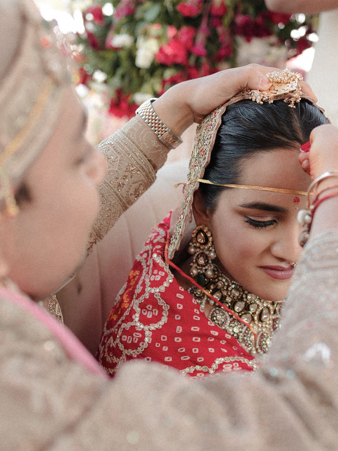 A bride in red lehenga gets her maang tikka placed during an Indian wedding ceremony.