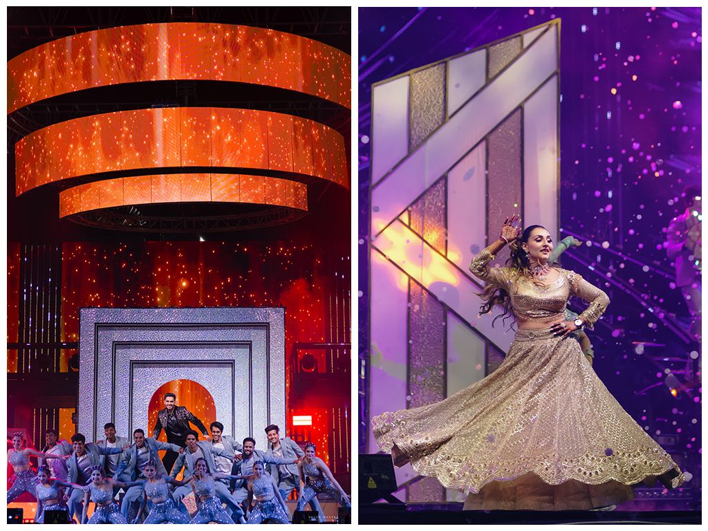 Indian wedding sangeet celebration with large group dance performance and bride twirling in golden lehenga on stage.