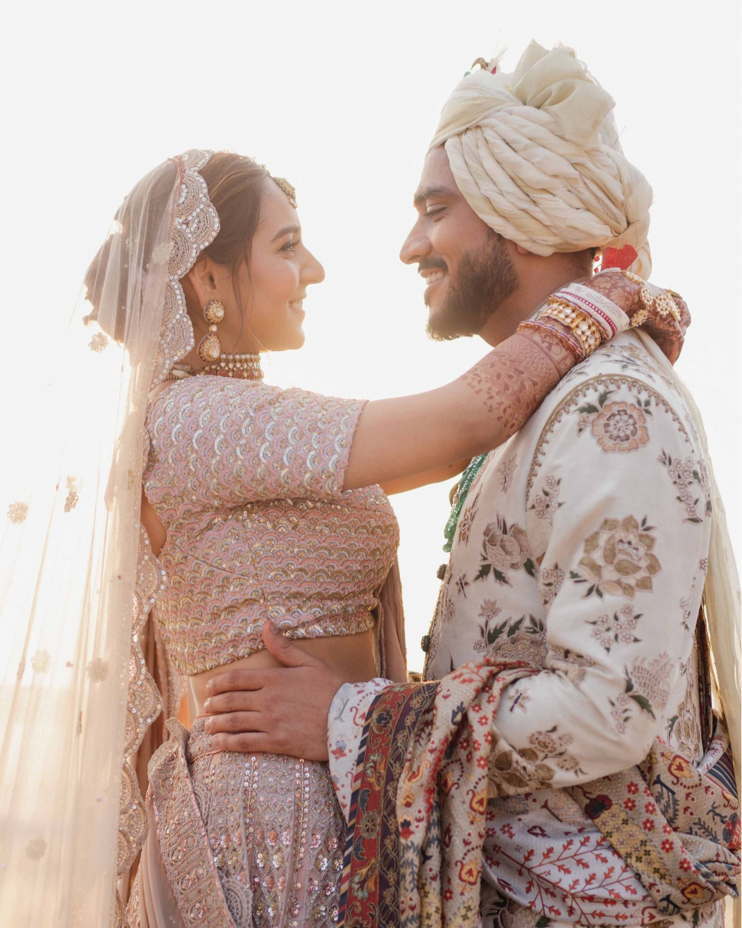 Indian bride and groom in traditional wedding attire share a romantic moment at golden hour.