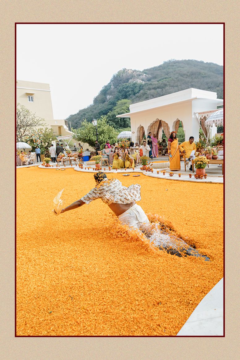 Man diving into a sea of marigold flowers at a vibrant outdoor Indian wedding haldi celebration.
