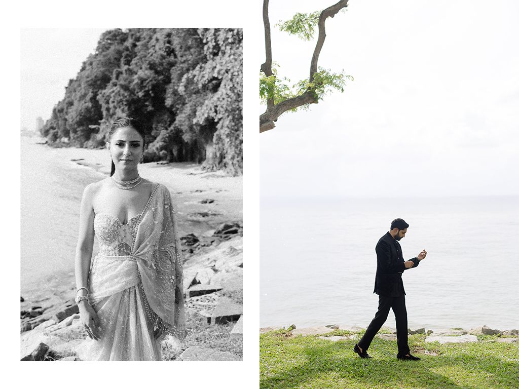 Bride in embellished saree poses on beach while groom walks along scenic Singapore coastline.