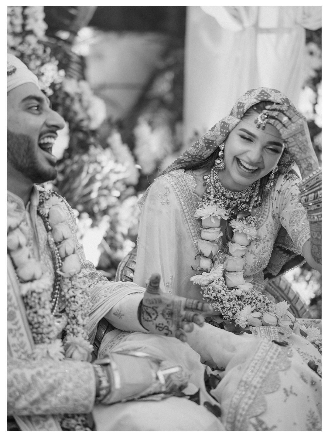 Black and white photo of Indian bride and groom laughing joyfully during wedding ceremony.