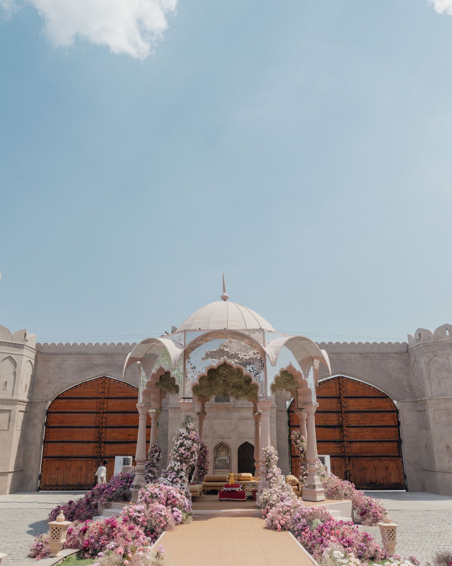 Stunning white Mughal-inspired wedding venue with pink floral decorations under blue sky.