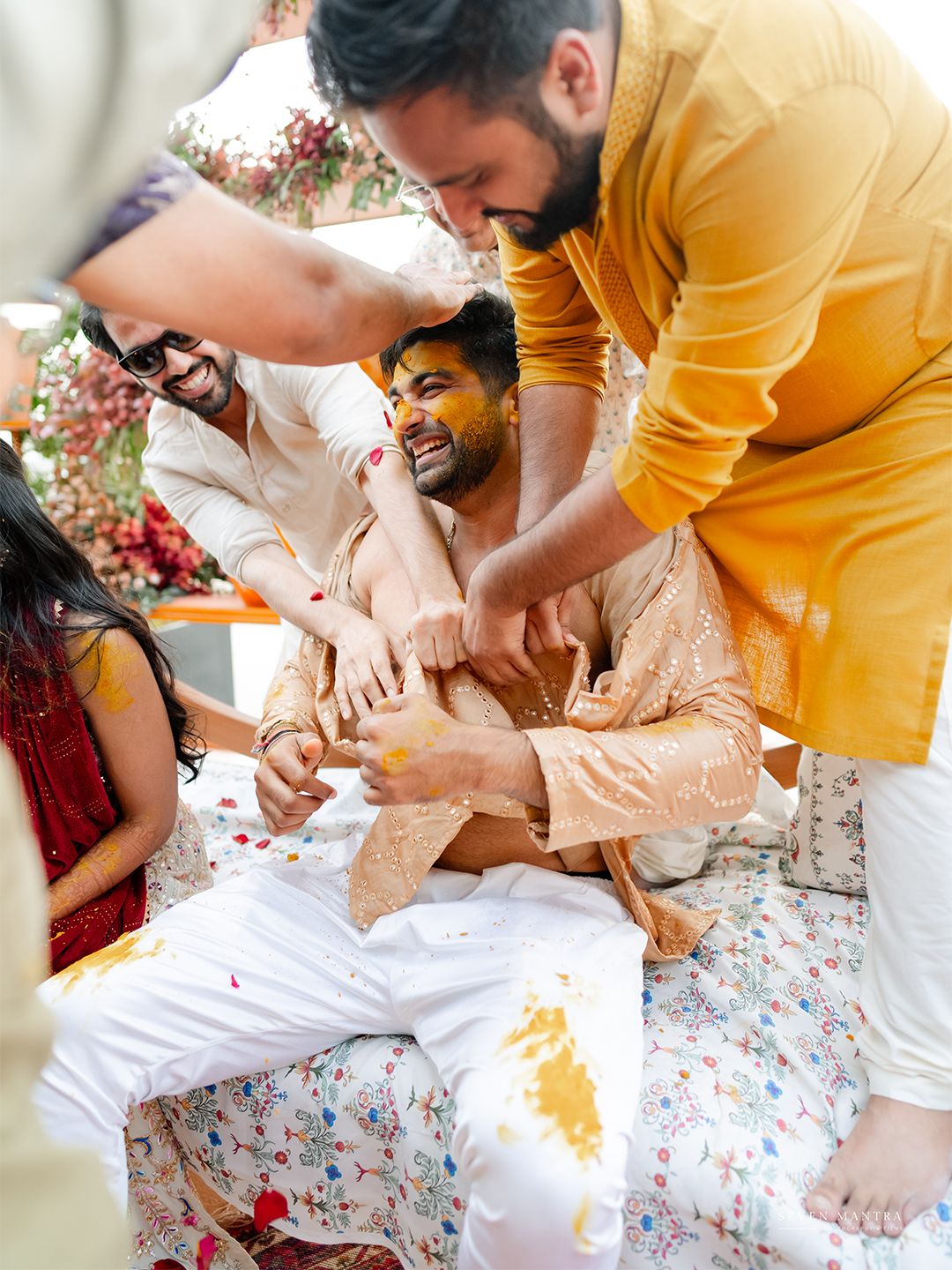 Groomsmen playfully apply Haldi turmeric paste to groom during Indian pre-wedding ritual.
