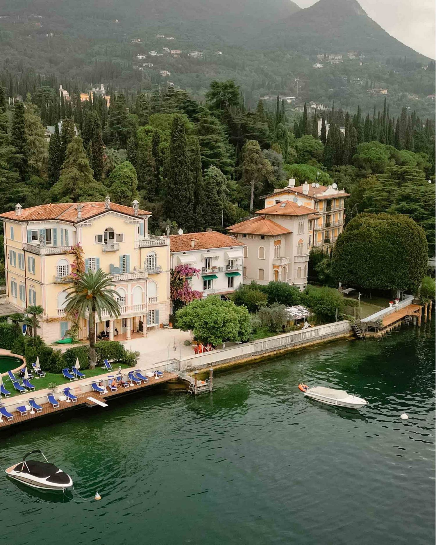 Aerial view of a luxury Italian lakeside villa with terracotta roofs surrounded by lush greenery.